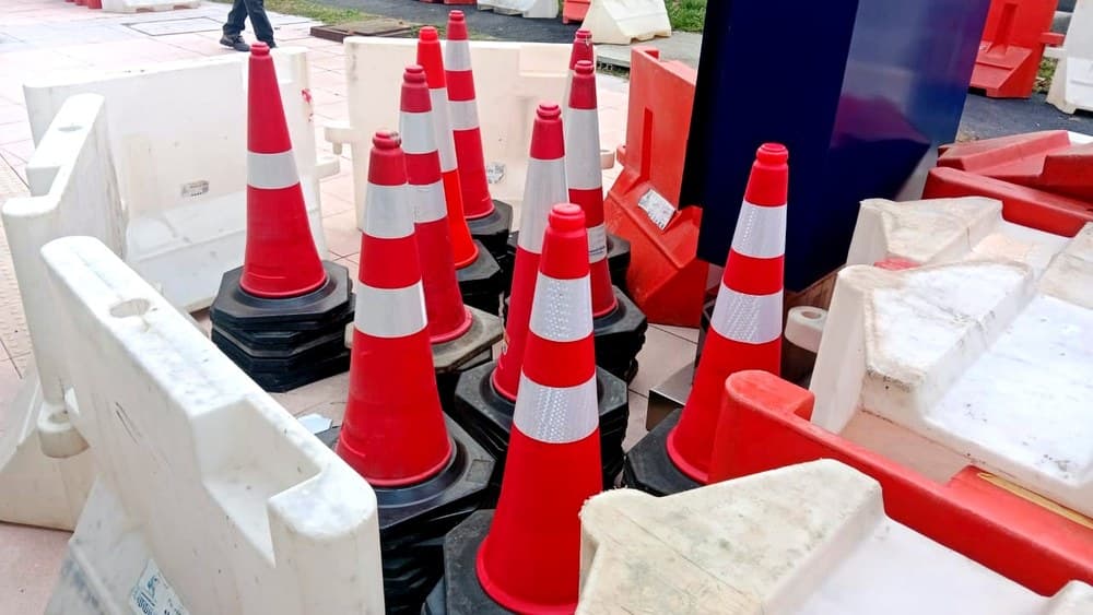 Traffic cones and red and white plastic barriers staged at an event site before a road closure.